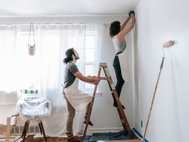 Man holds ladder as woman paints a room