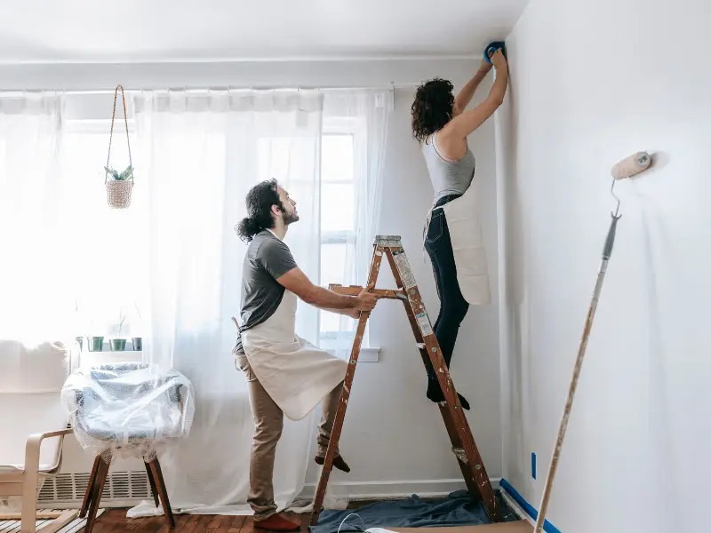 Man holds ladder as woman paints a room